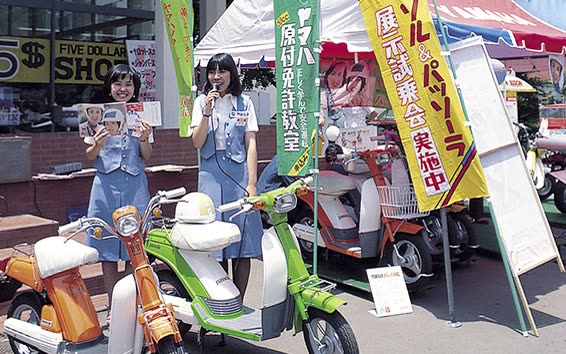 Hôtesses Yamaha présentant des Passol et Passola devant un magasin japonais, banderoles d'essais et de permis