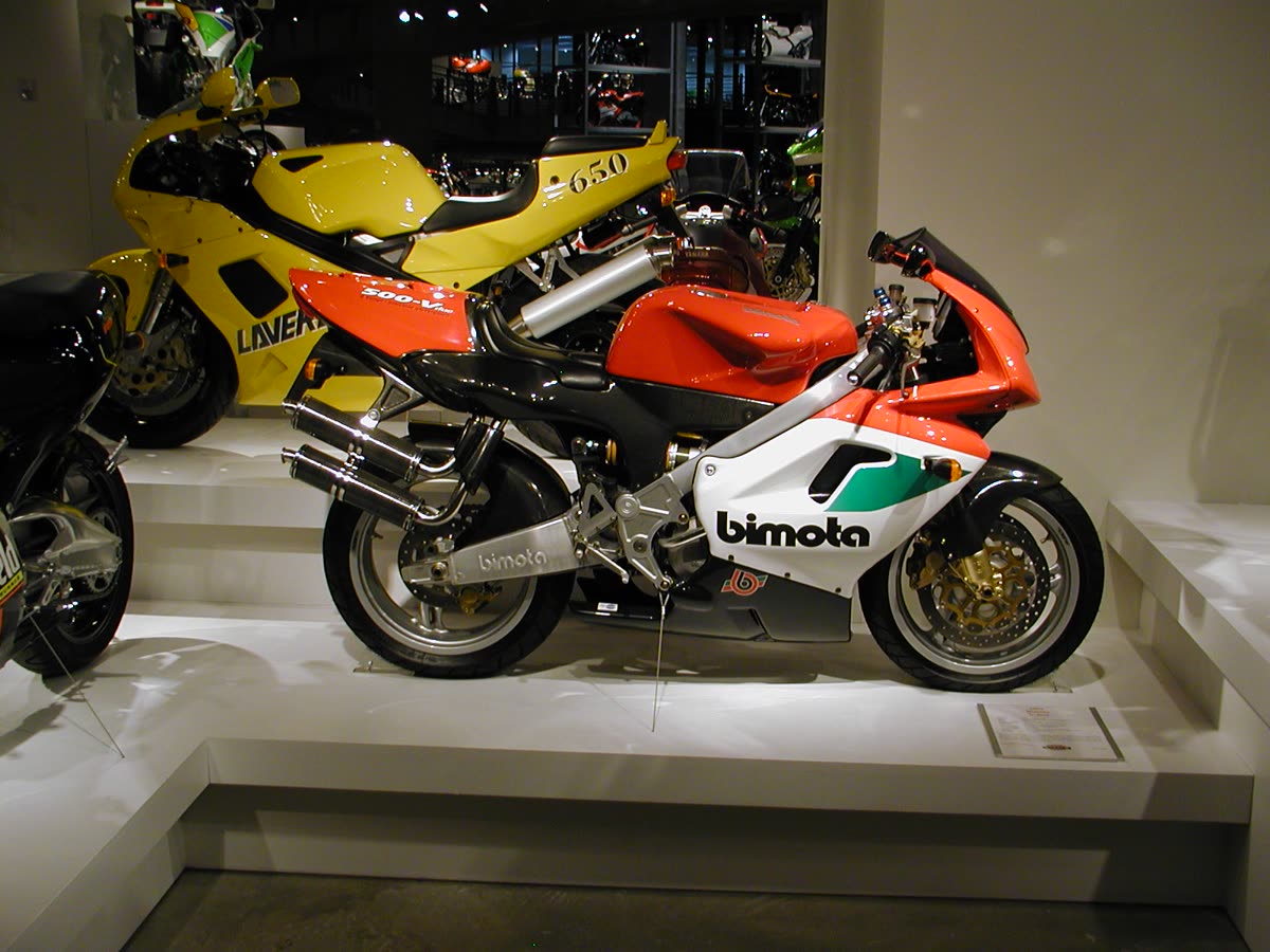 Bimota V-Due rouge, blanche et verte exposée sur le podium d'un musée, à côté d'une Laverda jaune