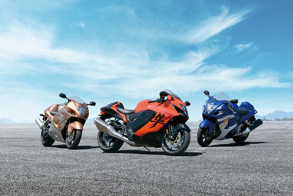 Trois Suzuki Hayabusa de générations successives, cuivre, orange et bleue, alignées sur un tarmac